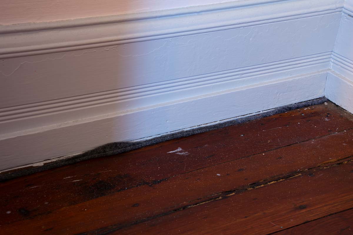 Gap between floorboards filled with felt weatherstripping.